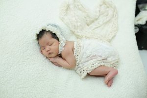 Adorable newborn baby sleeping peacefully in a soft, lace outfit on a cozy blanket.