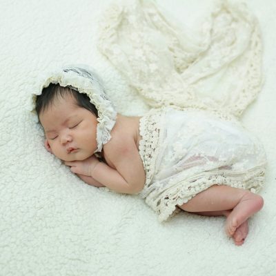 Adorable newborn baby sleeping peacefully in a soft, lace outfit on a cozy blanket.