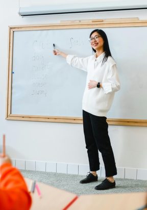 pexels photo 8466704 8466704 Smiling teacher instructing students in a classroom setting using a whiteboard.